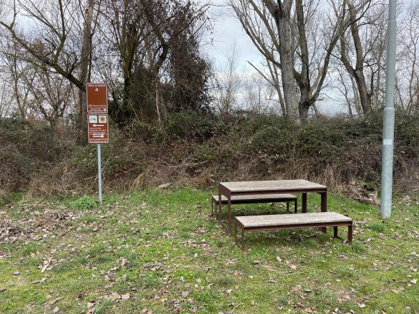 Outdoor rest area with table and two benches made of wood and metal. Brown sign with several directions on the path